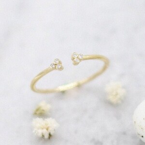 May include: A delicate gold ring with two small clusters of diamonds on the ends. The ring is open on one side, making it adjustable.