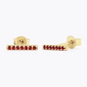 May include: A pair of gold bar earrings with red gemstones. The earrings are simple and elegant, perfect for everyday wear.