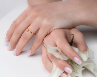 May include: A close-up of a hand wearing a gold ring with a small diamond. The hand is holding a white flower.