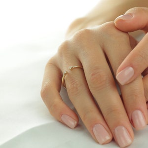 May include: A gold ring with two small diamonds on the top. The ring is on a person's finger.