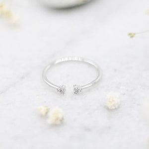 May include: A silver ring with a small cluster of clear stones on each side of the opening.