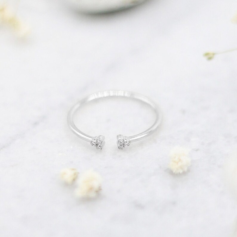 May include: A silver ring with a small cluster of clear stones on each side of the opening.