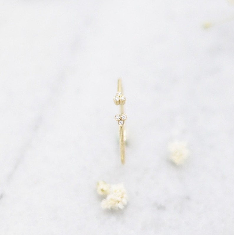 May include: A delicate gold ring with two clusters of small diamonds. The ring is simple and elegant, perfect for everyday wear.