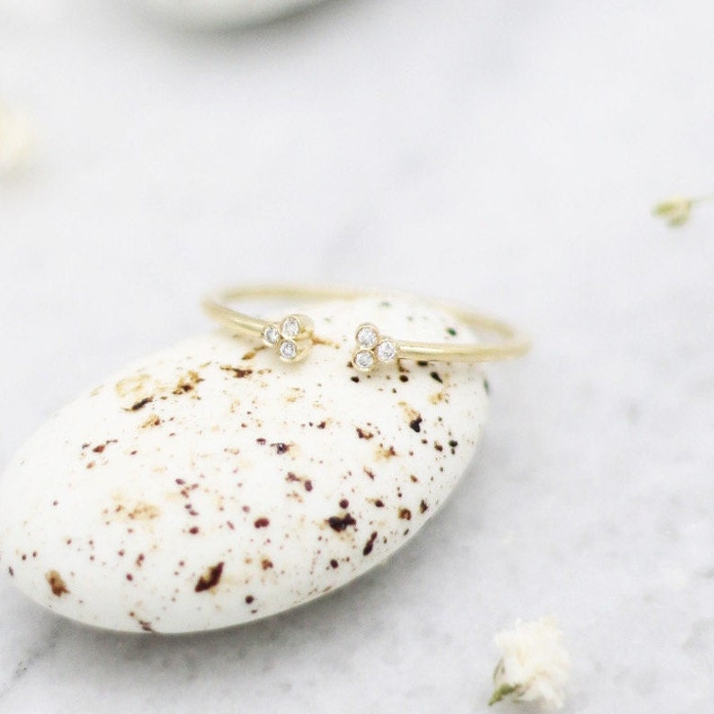 May include: A delicate gold ring with three small diamonds on each side. The ring is resting on a white stone with brown speckles.
