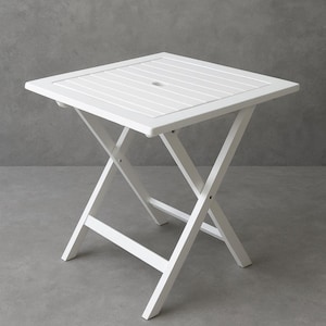 Può includere: Un tavolo pieghevole quadrato bianco per esterni. Il piano del tavolo ha un design a doghe con un piccolo foro al centro. Le gambe sono a forma di X, garantendo stabilità. Il tavolo è in legno e verniciato di bianco.