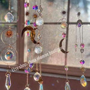Peut inclure: Des capteurs de soleil d&eacute;coratifs avec des prismes en cristal iris&eacute;s, des lunes et des soleils sont suspendus &agrave; de fines cha&icirc;nes. Les capteurs de soleil pr&eacute;sentent une vari&eacute;t&eacute; de formes et de tailles. Le texte "Etsy shop: elena monroe boutique" est visible.