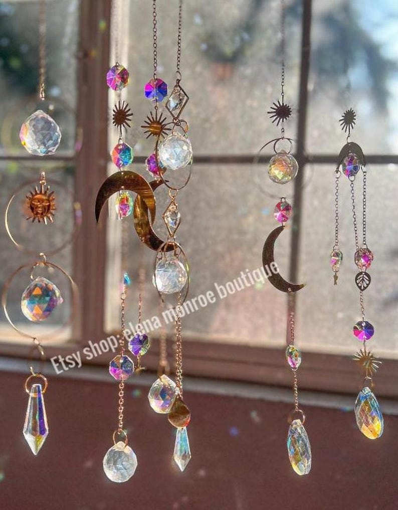 Peut inclure: Des capteurs de soleil d&eacute;coratifs avec des prismes en cristal iris&eacute;s, des lunes et des soleils sont suspendus &agrave; de fines cha&icirc;nes. Les capteurs de soleil pr&eacute;sentent une vari&eacute;t&eacute; de formes et de tailles. Le texte "Etsy shop: elena monroe boutique" est visible.