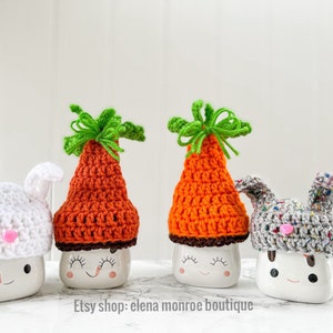 May include: Four white ceramic mugs with different crocheted hats. The hats are a white bunny, an orange carrot, a gray bunny, and a multi-colored bunny. The mugs have painted eyes and smiles. Etsy shop: elena monroe boutique