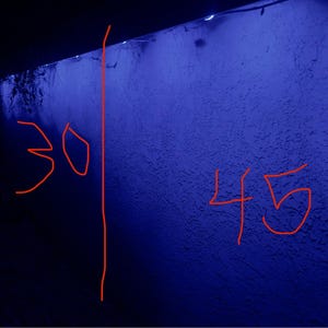 K&ouml;nnte beinhalten: Eine strukturierte blaue Wand mit den Zahlen 30 und 45 in Rot gezeichnet. Eine vertikale rote Linie trennt die beiden Zahlen. Die Wand befindet sich unter einem dunklen Vordach.