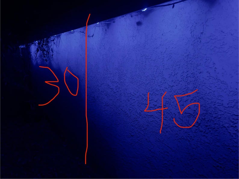 K&ouml;nnte beinhalten: Eine strukturierte blaue Wand mit den Zahlen 30 und 45 in Rot gezeichnet. Eine vertikale rote Linie trennt die beiden Zahlen. Die Wand befindet sich unter einem dunklen Vordach.