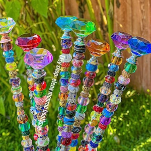 May include: A set of seven colorful crystal topped garden stakes, each with a different colored crystal top and a string of colorful beads. The beads are a mix of glass, metal, and plastic.