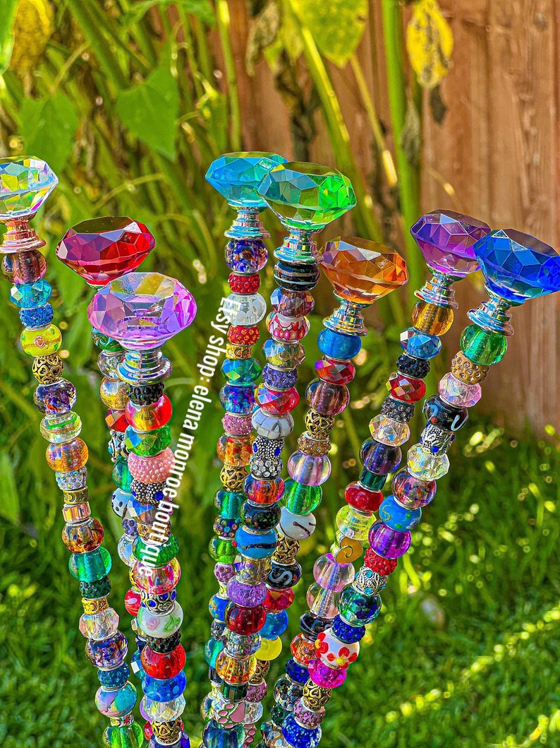 May include: A set of seven colorful crystal topped garden stakes, each with a different colored crystal top and a string of colorful beads. The beads are a mix of glass, metal, and plastic.