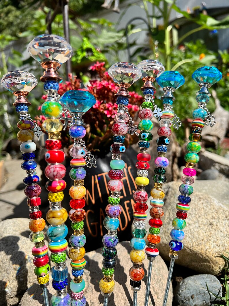 May include: A set of seven colorful garden stakes with crystal tops and beads. The stakes are decorated with various colors, including red, blue, green, yellow, and purple. The beads are made of glass and have a variety of shapes and sizes. The stakes are about 12 inches long.