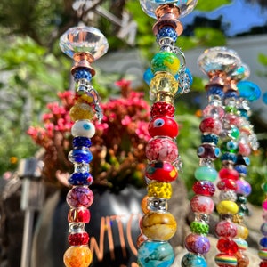 May include: A set of colorful beaded garden stakes with crystal tops. The beads are various colors, including red, blue, green, yellow, and orange. The stakes are made of metal and have a silver finish. The crystal tops are clear and have a faceted design.