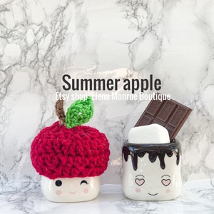 May include: Two white ceramic mugs shaped like marshmallows with smiling faces. One mug has a red crocheted apple hat on top and the other mug has a chocolate bar and a white marshmallow on top. The mugs are on a white marble background. The text "Summer apple" and "Etsy shop Elena Monroe Boutique" is written above the mugs.