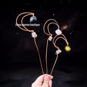May include: Handmade copper wire hair accessories with gemstone and charm accents. One features a dark blue stone, another a pink stone, and a yellow sun charm. The text "Elena monroe boutique" is visible.