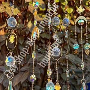 Peut inclure: Suncatchers d&eacute;coratifs suspendus avec des pendentifs en cristal iris&eacute;, des breloques soleil, lune et &eacute;toile, suspendus par des cha&icirc;nes dor&eacute;es. L'image comprend le texte "etsy shop: elena monroe boutique".