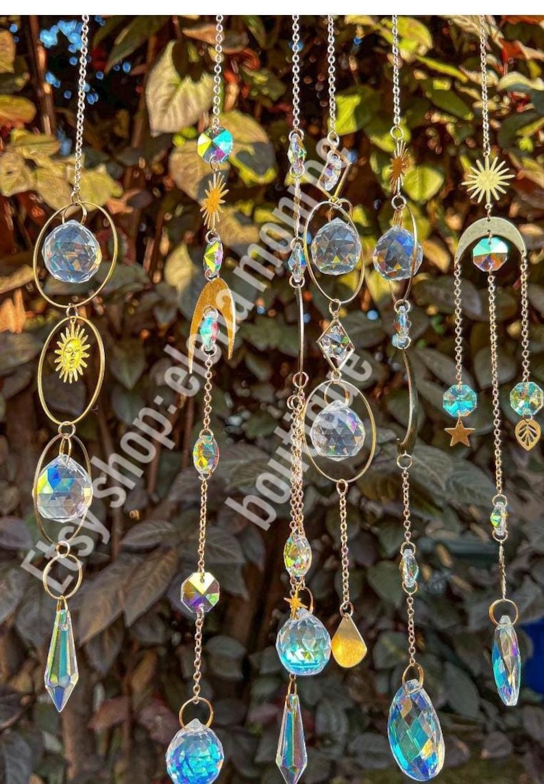 Peut inclure: Suncatchers d&eacute;coratifs suspendus avec des pendentifs en cristal iris&eacute;, des breloques soleil, lune et &eacute;toile, suspendus par des cha&icirc;nes dor&eacute;es. L'image comprend le texte "etsy shop: elena monroe boutique".