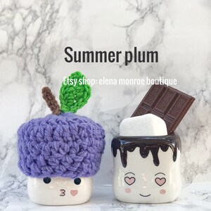 May include: Two ceramic mugs shaped like marshmallows with faces. One mug has a purple crocheted hat shaped like a plum with a green leaf. The other mug has a chocolate bar and a white marshmallow on top. The text "Summer plum" and "Etsy shop: elena monroe boutique" is on the background.