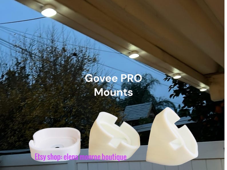 K&ouml;nnte beinhalten: Wei&szlig;e Govee PRO-Halterungen in verschiedenen Formen werden vor dem Hintergrund eines bew&ouml;lkten Himmels und Bl&auml;ttern gezeigt. Der Text "Govee PRO Mounts" ist sichtbar. Der Etsy-Shop-Name "elena monroe boutique" ist ebenfalls sichtbar.