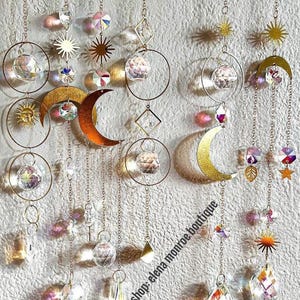 Peut inclure: Ornements d&eacute;coratifs suspendus avec des th&egrave;mes c&eacute;lestes. La conception comprend des soleils, des lunes et des formes g&eacute;om&eacute;triques dor&eacute;s, ainsi que des sph&egrave;res de cristal transparentes et des cristaux facett&eacute;s. Les ornements sont suspendus par de fines cha&icirc;nes.