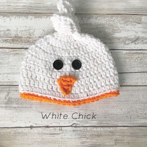 K&ouml;nnte beinhalten: Wei&szlig;e H&auml;kelm&uuml;tze f&uuml;r Babys mit orangem Saum und schwarzen Knopfaugen. Die M&uuml;tze ist in Form eines K&uuml;ken mit einem orangefarbenen Schnabel geformt.