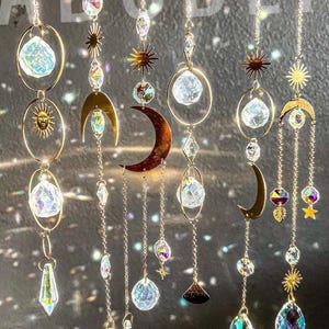 Peut inclure: Suncatchers d&eacute;coratifs en cristal suspendus avec des motifs c&eacute;lestes. Chaque capteur de soleil comprend une cha&icirc;ne dor&eacute;e, une boule de cristal transparente et divers breloques, dont des soleils, des lunes et des &eacute;toiles. Les cristaux r&eacute;fractent la lumi&egrave;re.