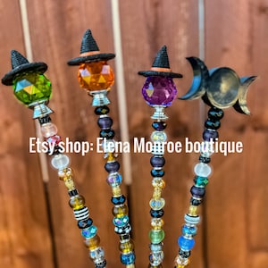 Pode incluir: Quatro varinhas decorativas com tampas de cristal facetadas coloridas e cabos de contas. Cada varinha apresenta um pequeno chapéu de bruxa preto. O texto "Etsy shop: Elena Monroe boutique" é visível.
