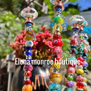 May include: Decorative beaded garden stakes with crystal tops. The stakes are adorned with a variety of colourful glass beads. The text "Elena monroe boutique" is visible. The beads are in shades of red, blue, yellow, and green.