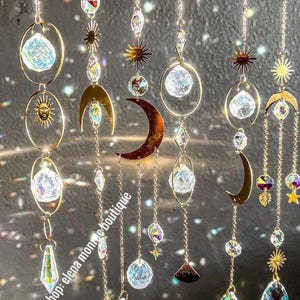 Peut inclure: Suncatchers d&eacute;coratifs suspendus avec des soleils, des lunes et des &eacute;clats d'&eacute;toiles en m&eacute;tal dor&eacute;. Les capteurs solaires pr&eacute;sentent des cristaux clairs et facett&eacute;s et sont suspendus par de fines cha&icirc;nes. Le nom de la boutique Etsy "elena monroe boutique" est imprim&eacute;.