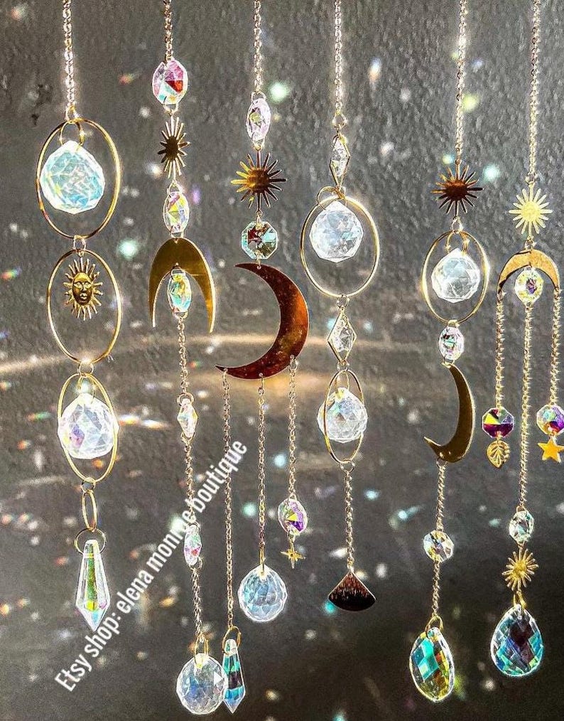 Peut inclure: Suncatchers d&eacute;coratifs suspendus avec des soleils, des lunes et des &eacute;clats d'&eacute;toiles en m&eacute;tal dor&eacute;. Les capteurs solaires pr&eacute;sentent des cristaux clairs et facett&eacute;s et sont suspendus par de fines cha&icirc;nes. Le nom de la boutique Etsy "elena monroe boutique" est imprim&eacute;.