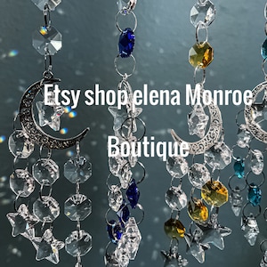 May include: A crystal suncatcher with silver crescent moons and stars, featuring blue, clear, and amber crystals. The suncatcher is labeled "Etsy shop elena Monroe Boutique".
