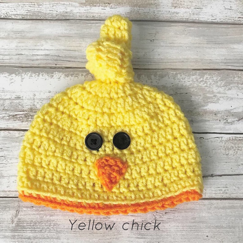 K&ouml;nnte beinhalten: Gelber H&auml;kel-Babyhut in Form eines K&uuml;ken mit schwarzen Knopfaugen, einem orangefarbenen Schnabel und einem orangefarbenen H&auml;kelrand.