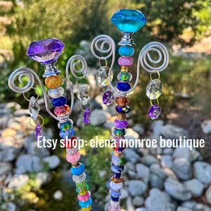 May include: Two colorful beaded wands with crystal accents and a silver wire design. The wands are topped with a purple and a blue crystal.
