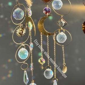 Peut inclure: Attrape-soleil c&eacute;lestes dor&eacute;s avec des accents de cristal. Chaque capteur de soleil pr&eacute;sente un soleil, une lune et des sph&egrave;res de cristal, suspendus par de fines cha&icirc;nes. Le texte "Etsy shop: elena monroe boutique" est visible.