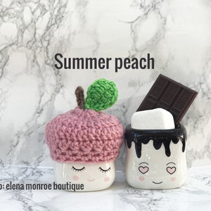 May include: Two ceramic mugs shaped like marshmallows with faces. One mug is wearing a pink crocheted hat with a green leaf on top. The other mug has chocolate syrup dripping down the side and a chocolate bar on top. The text "Summer peach" is above the mugs. The text "Etsy shop: elena monroe boutique" is below the mugs.