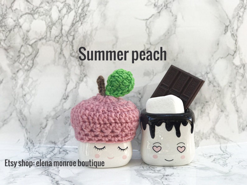 May include: Two ceramic mugs shaped like marshmallows with faces. One mug is wearing a pink crocheted hat with a green leaf on top. The other mug has chocolate syrup dripping down the side and a chocolate bar on top. The text "Summer peach" is above the mugs. The text "Etsy shop: elena monroe boutique" is below the mugs.