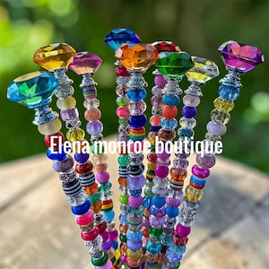 May include: A collection of colorful beaded pens with faceted gemstone tops. The pens feature a variety of bead colors, including blue, pink, orange, and green. The text "Elena monroe boutique" is visible.