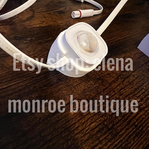 K&ouml;nnte beinhalten: Ein wei&szlig;es elektrisches Bauteil mit einer klaren, abgerundeten Linse, verbunden mit wei&szlig;en Kabeln. Der Text "Etsy shop lena" und "monroe boutique" sind sichtbar. Das Objekt liegt auf einer dunkelbraunen Holzoberfl&auml;che.