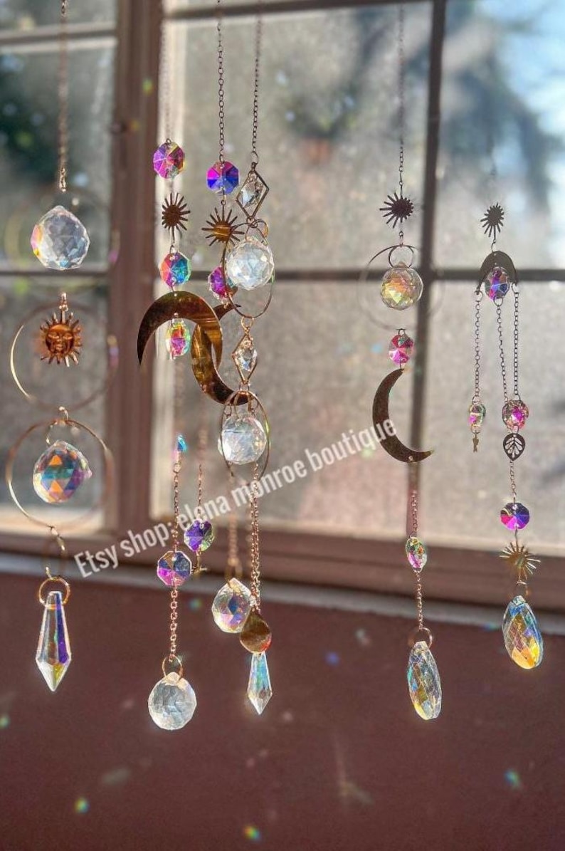 Peut inclure: Suns-catchers d&eacute;coratifs suspendus avec des prismes en cristal transparent, des cristaux iris&eacute;s et des soleils, lunes et &eacute;toiles en m&eacute;tal dor&eacute;. Les attrape-soleil sont suspendus par de fines cha&icirc;nes, cr&eacute;ant un affichage sur le th&egrave;me c&eacute;leste.