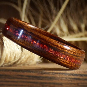 Peut inclure: Une bague en bois brun foncé avec un incrustation de paillettes rouges. La bague est polie et a une finition lisse.