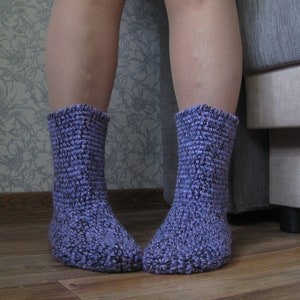 Puede incluir: Un par de calcetines de punto morado con un patrón texturizado. Los calcetines se llevan puestos en los pies de una persona.
