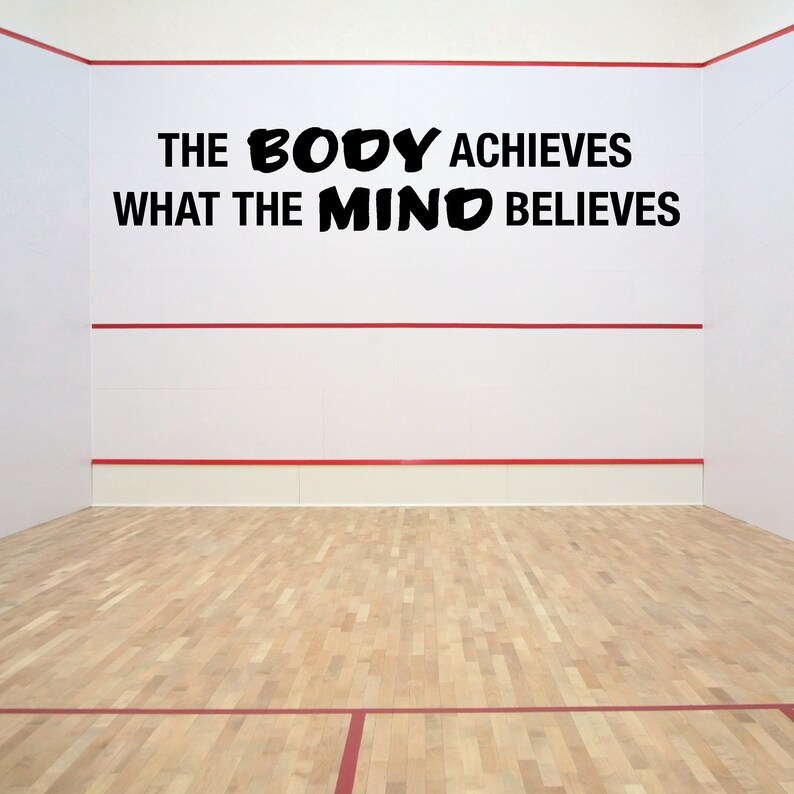 May include: A white wall with a red line across the middle. The wall has a black motivational quote that reads "The body achieves what the mind believes". The wall is in a squash court with a wooden floor.
