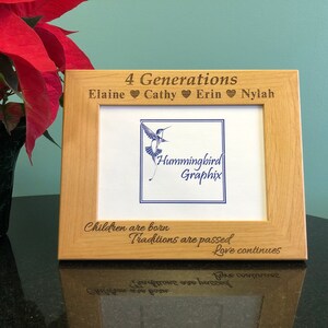 May include: A wooden picture frame with an engraved inscription that reads "4 Generations Elaine Cathy Erin Nylah". The frame also features a hummingbird graphic and the text "Hummingbird Graphix". The bottom of the frame has the engraved text "Children are born Traditions are passed Love continues".
