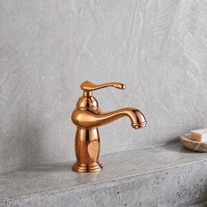 May include: A polished copper-toned bathroom tap with a single curved handle and a rounded spout. The tap features a smooth, reflective metallic finish and a classic, rounded base design, standing upright with a prominent, elegant arch.