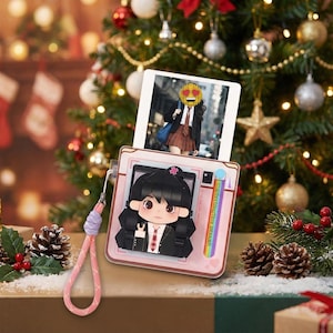 Peut inclure: Un cadre photo rose et blanc avec un personnage de dessin animé et une photo d'une personne portant un blazer et une jupe. Le cadre a une sangle rose, avec un sapin de Noël en arrière-plan.