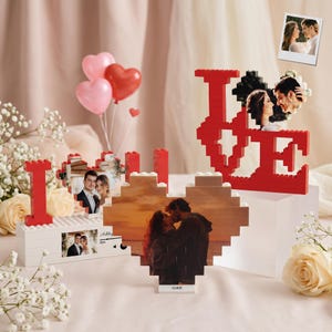 Peut inclure: Présentation de cadeaux photo personnalisés, dont le mot "LOVE" construit avec des blocs de construction rouges. Les cadeaux présentent des photos de couples, avec des ballons en forme de cœur et des fleurs ajoutant au thème romantique. Une petite photo est également incluse.