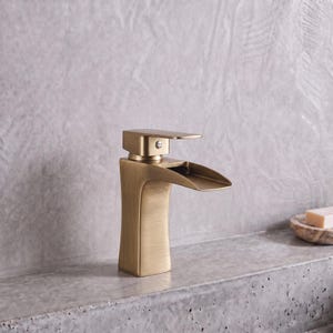 Könnte beinhalten: Eine Einhebel-Waschtischarmatur mit gebürstetem Messing-Finish und einem breiten, flachen Wasserfall-Auslauf. Die Armatur verfügt über einen rechteckigen Sockel, der sich nach oben leicht verjüngt, sowie eine kleine kreisförmige Anzeige.