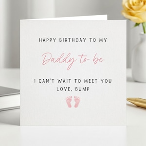 Pode incluir: Um cartão branco com o texto "HAPPY BIRTHDAY TO MY Daddy to be I CAN'T WAIT TO MEET YOU LOVE, BUMP" em letras pretas e rosa. O cartão apresenta duas pegadas de bebé cor-de-rosa. Uma rosa amarela num vaso branco no fundo.