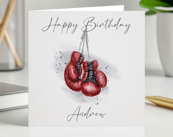 May include: A greeting card with the words "Happy Birthday" and "Andrew" in elegant script. The card features a watercolor illustration of red boxing gloves hanging from a string, with black splatter accents.
